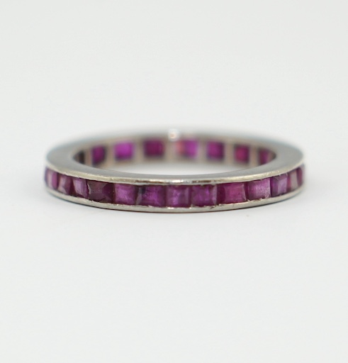 A white metal and rectangular cut ruby set full eternity ring, size M/N, gross weight 3.5 grams. Condition - fair